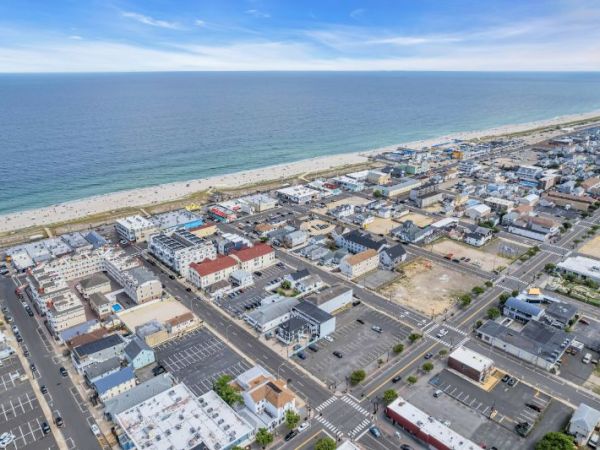 Aerial view of a coastal town with buildings, streets, and a sandy beach next to the ocean under a blue sky.